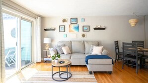 Una sala de estar con un sofá, una mesa de centro, una mesa de comedor con sillas y obras de arte en la pared.