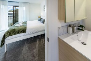 Une chambre d’hôtel moderne, équipée d’un lit, d’une salle de bain avec un lavabo et un miroir, et offrant une vue sur l’extérieur.