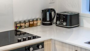 Una cocina con una cafetera negra, un tostador y varios frascos de especias sobre una encimera blanca.