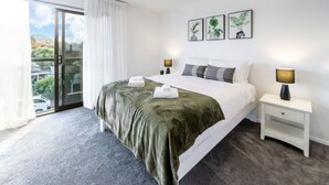 Habitación de hotel con una cama grande, dos mesitas de noche, un ventanal corredero al balcón y tres cuadros en la pared.