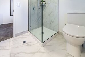 Un baño con cabina de ducha de vidrio, inodoro blanco y suelo de mármol.