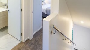 Un intérieur moderne avec un escalier recouvert de moquette, une salle de bain ouverte dotée d’un miroir et d’un lavabo, et une chambre à coucher avec un lit et des oreillers.