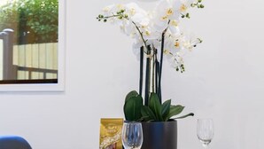 Un coin repas avec une table ronde, des assiettes blanches, un verre à vin, un bol, une plante en pot et une horloge au mur.