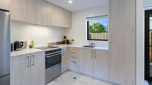 A modern kitchen with light wood cabinets, stainless steel appliances, and a large window providing a view of the outdoors.