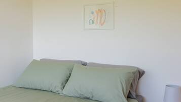 A single bed with a green bedspread and pillows, a wooden nightstand with a lamp, and a framed picture on the wall.