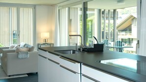 Een moderne keuken met een groot raam, een zithoek met een tafel en stoelen, en een bank met een plaids.