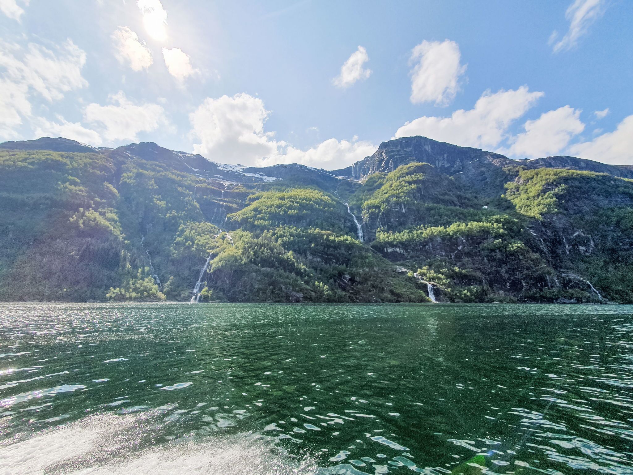 Un lago de aguas cristalinas que refleja el cielo, rodeado de montañas verdes y exuberantes cascadas.