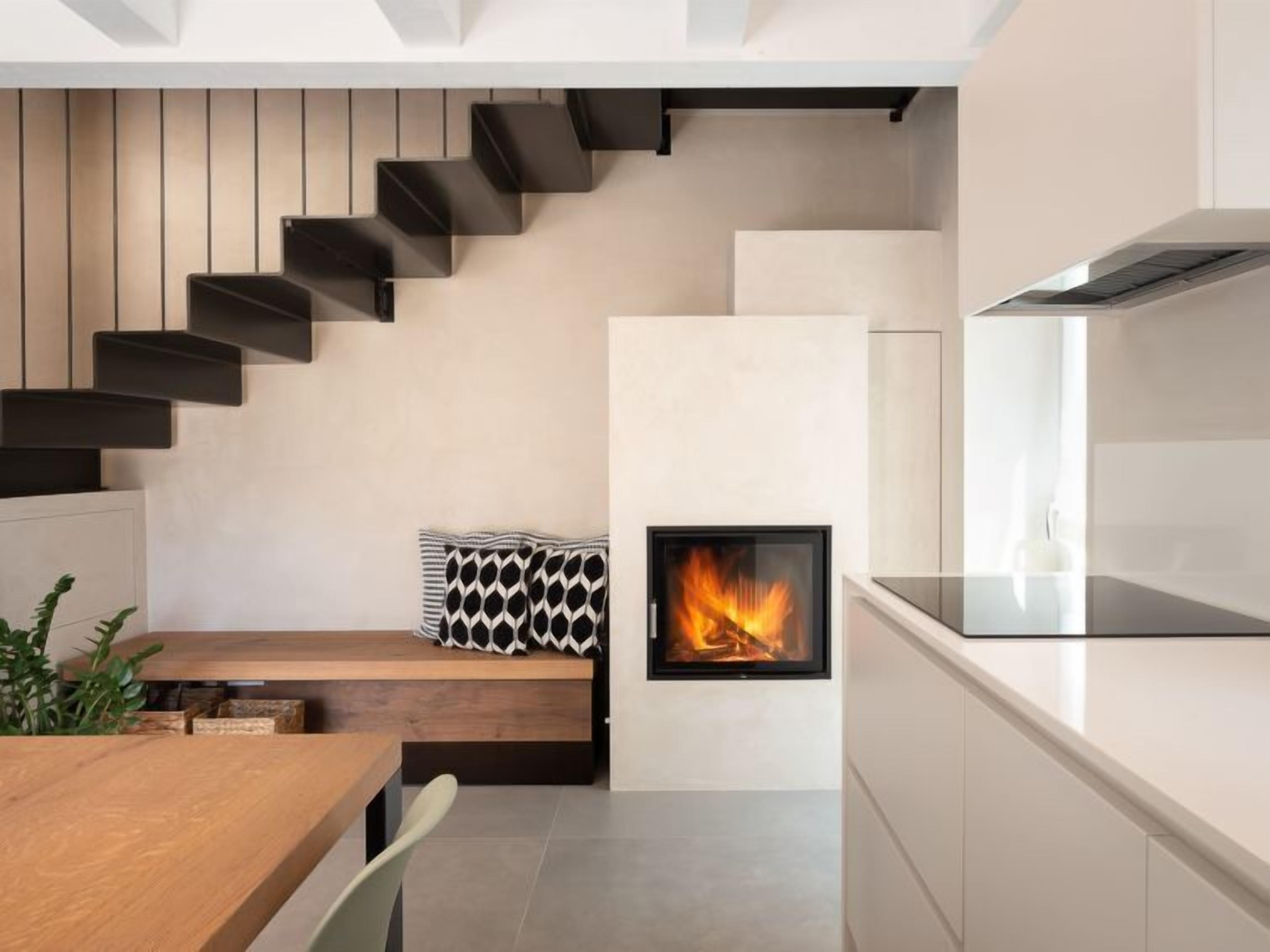 Een moderne keuken met een ingebouwde open haard, een houten eettafel en een trap met zwarte treden.
