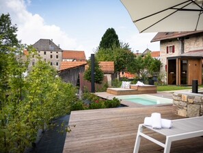 A wooden deck with a pool, a lounge chair, and a stone wall.