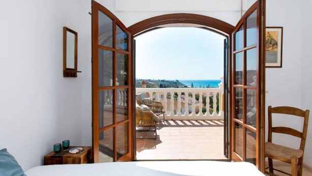 Une chambre avec un grand lit, une chaise en bois et un balcon donnant sur la mer.