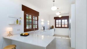Une cuisine moderne dotée d’un îlot central, de tabourets en bois, de luminaires suspendus et offrant une vue par la fenêtre.
