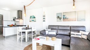 Een moderne woonkamer met een grijze bank, een witte eettafel en een keuken op de achtergrond.