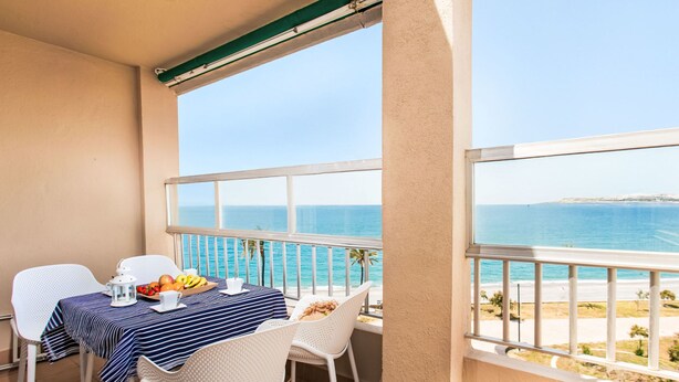 Een balkon met een tafel gedekt voor twee, met uitzicht op een strand en de zee.