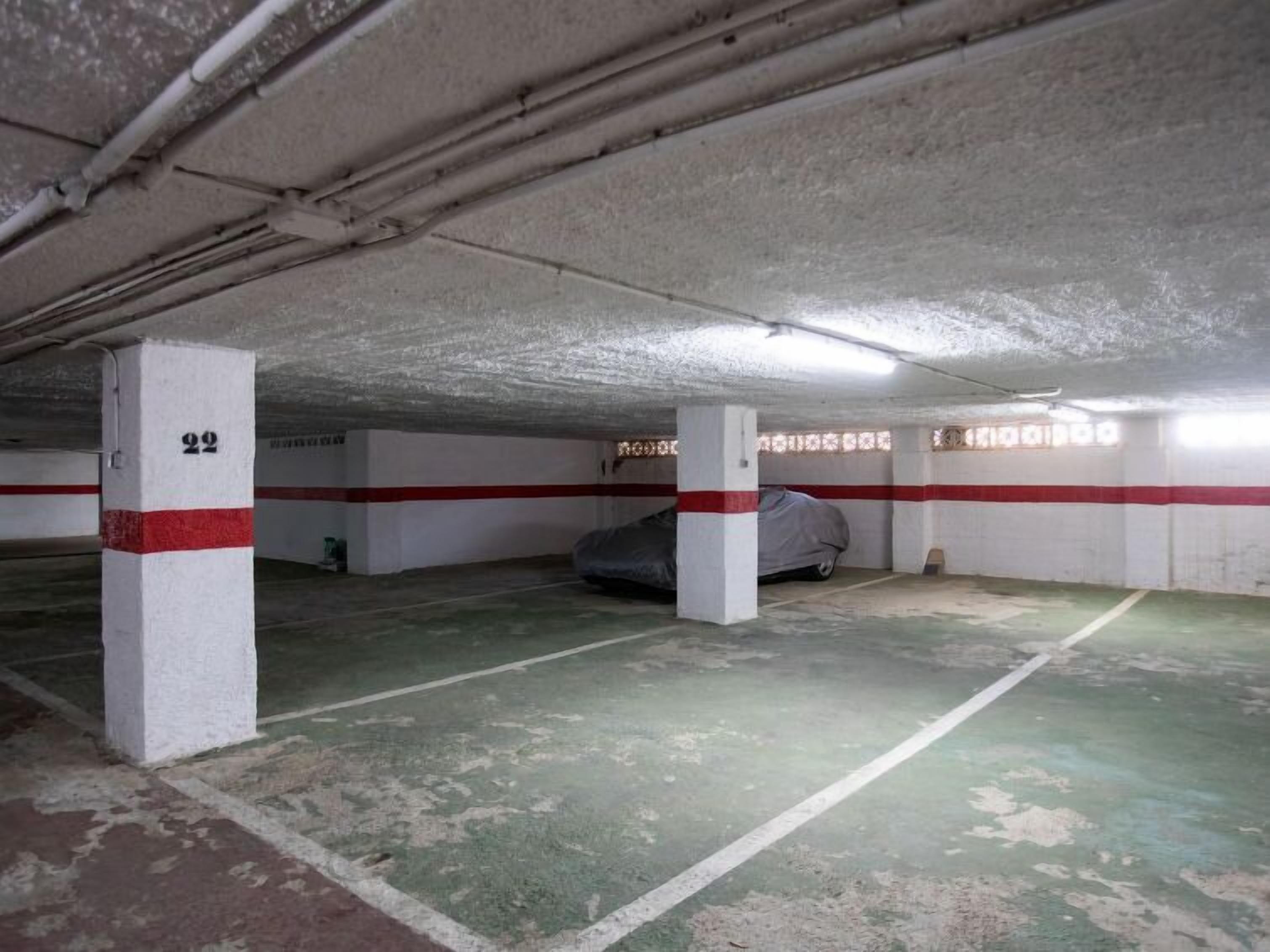 Eine Parkgarage mit Betonsäulen, grünen Markierungsstreifen und einem Auto, das mit einer Plane abgedeckt ist.