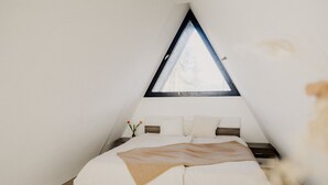 Een kamer met een driehoekige vorm, voorzien van een dakraam, een bed met witte beddengoed en een houten vloer.
