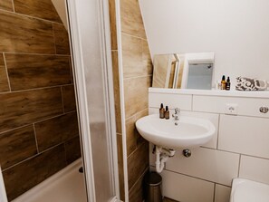 Un bagno con doccia, lavandino e specchio. Sul ripiano del lavandino sono presenti articoli da toilette.