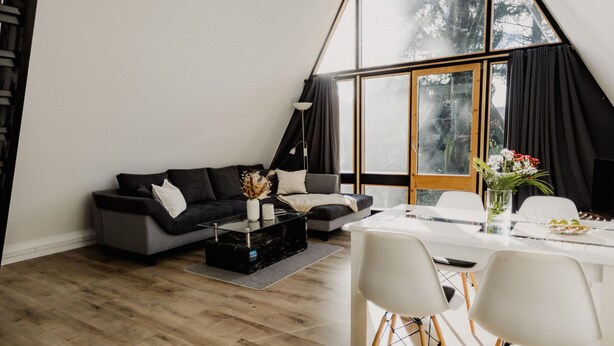 Een moderne woonkamer met een zwarte bank, een glazen salontafel, en een eethoek met witte stoelen en een glazen tafel.