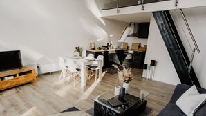 Een moderne woonkamer met een bank, salontafel en tv-meubel. Er is een eethoek met een tafel en stoelen. In de achtergrond is een keuken zichtbaar.