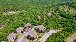 Vista aérea de una zona residencial con varias casas de dos pisos, un estacionamiento y una carretera sinuosa que atraviesa un paisaje boscoso.