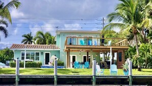 Une maison à deux étages avec un balcon, une piscine et une jetée qui s’avance dans un plan d’eau.
