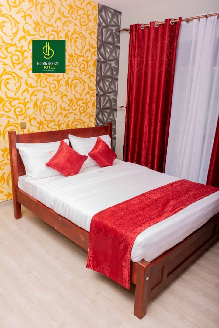 Habitación de hotel con cama de madera, cortinas rojas y blancas y un papel tapiz estampado.
