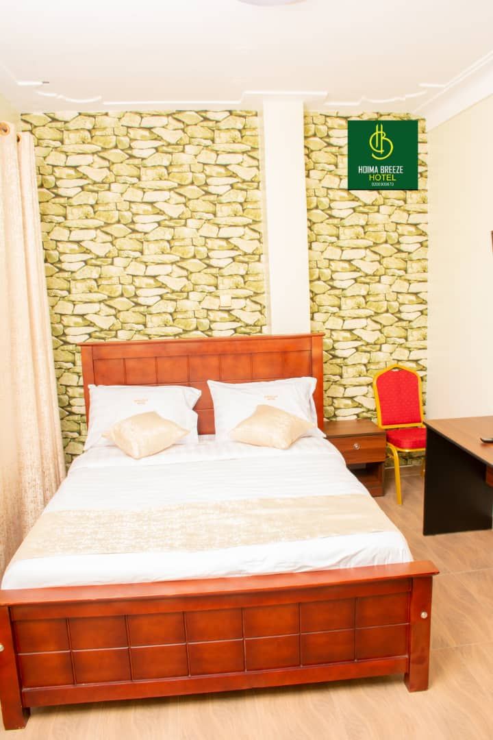 A hotel room with a stone wall, a wooden bed, a red chair, and a sign for the hotel.