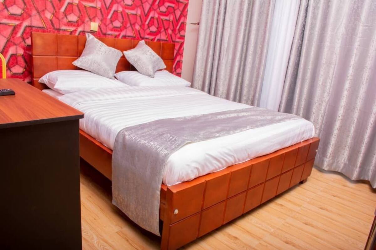 Un lit avec une tête de lit en bois, une literie blanche et une couverture grise.
