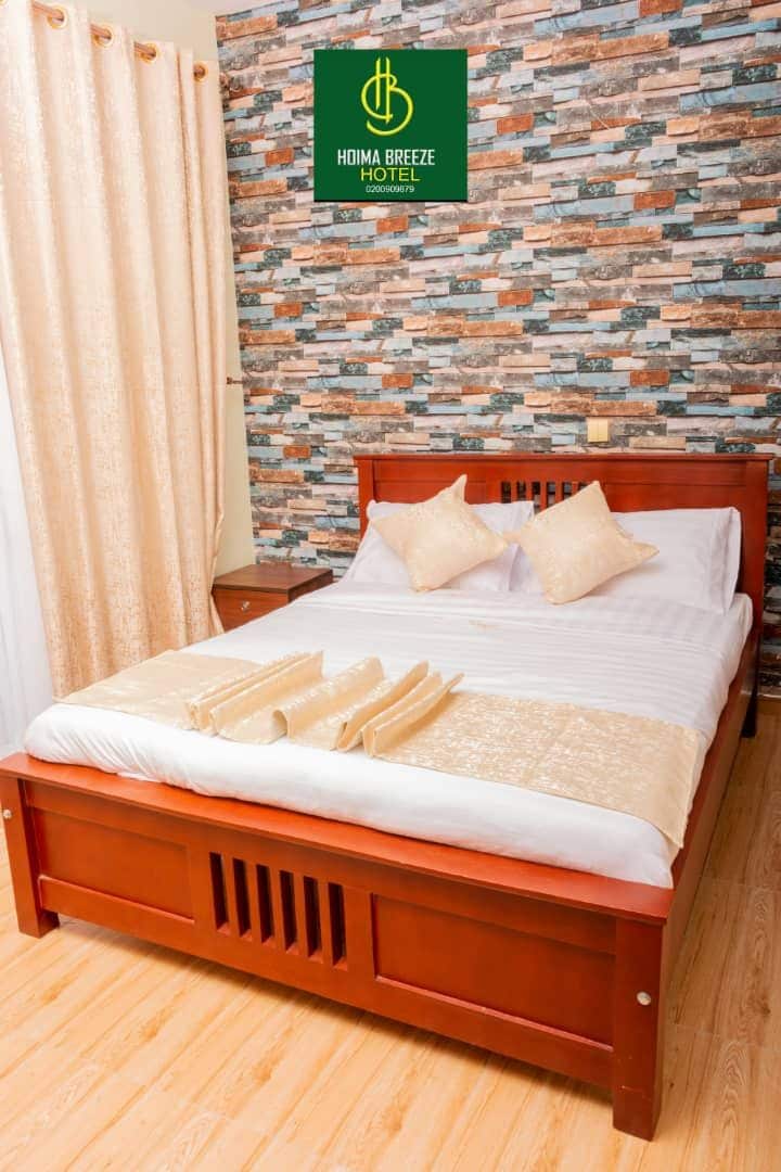 A hotel room with a wooden bed, a patterned wall, and a curtain.
