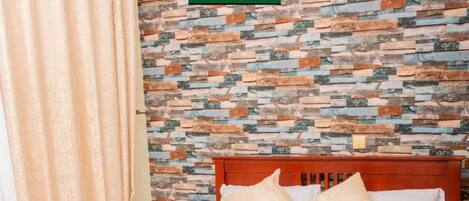 A hotel room with a wooden bed, a patterned wall, and a curtain.