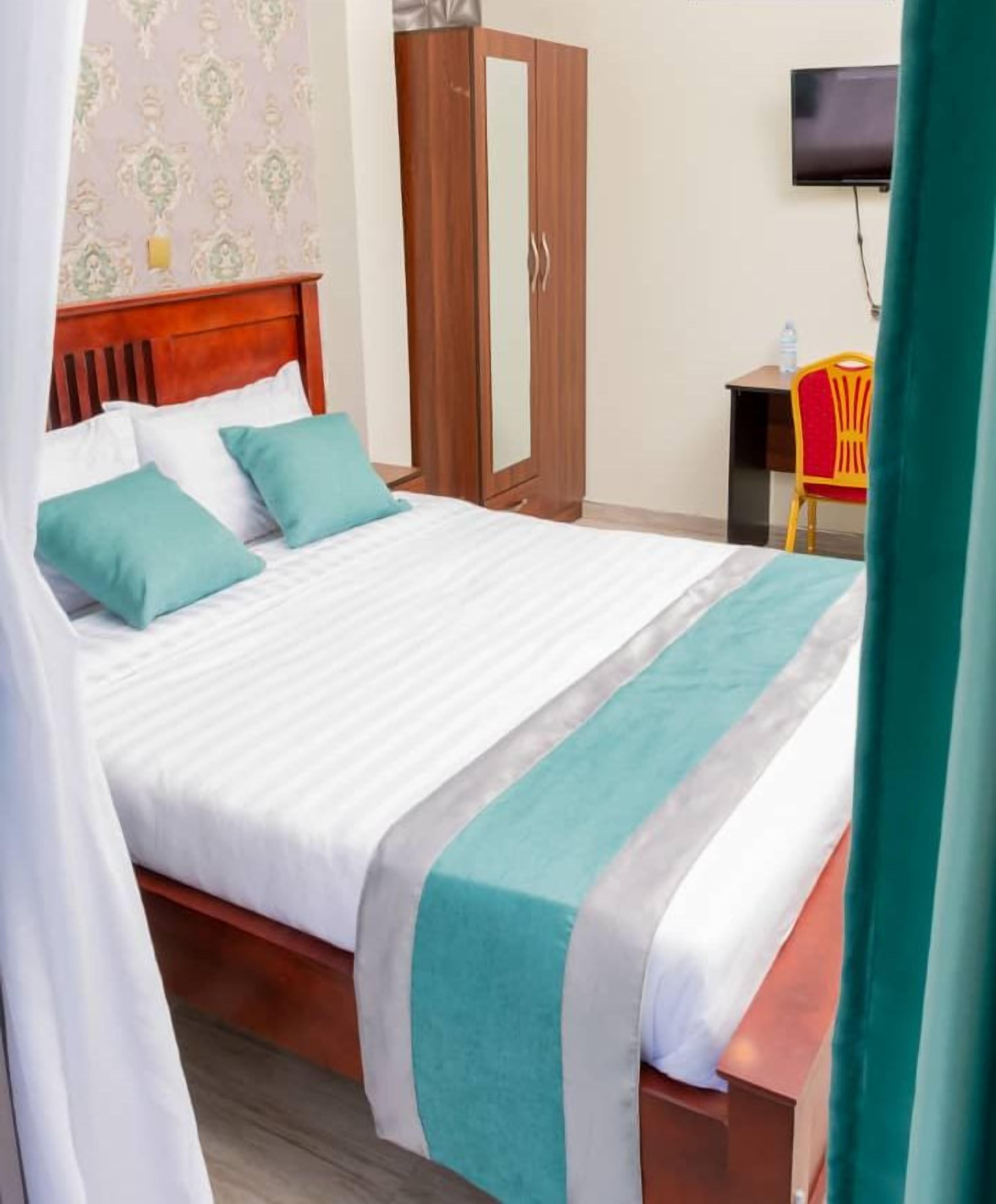 Quarto de hotel com cama, guarda-roupa, escrivaninha e televisão.
