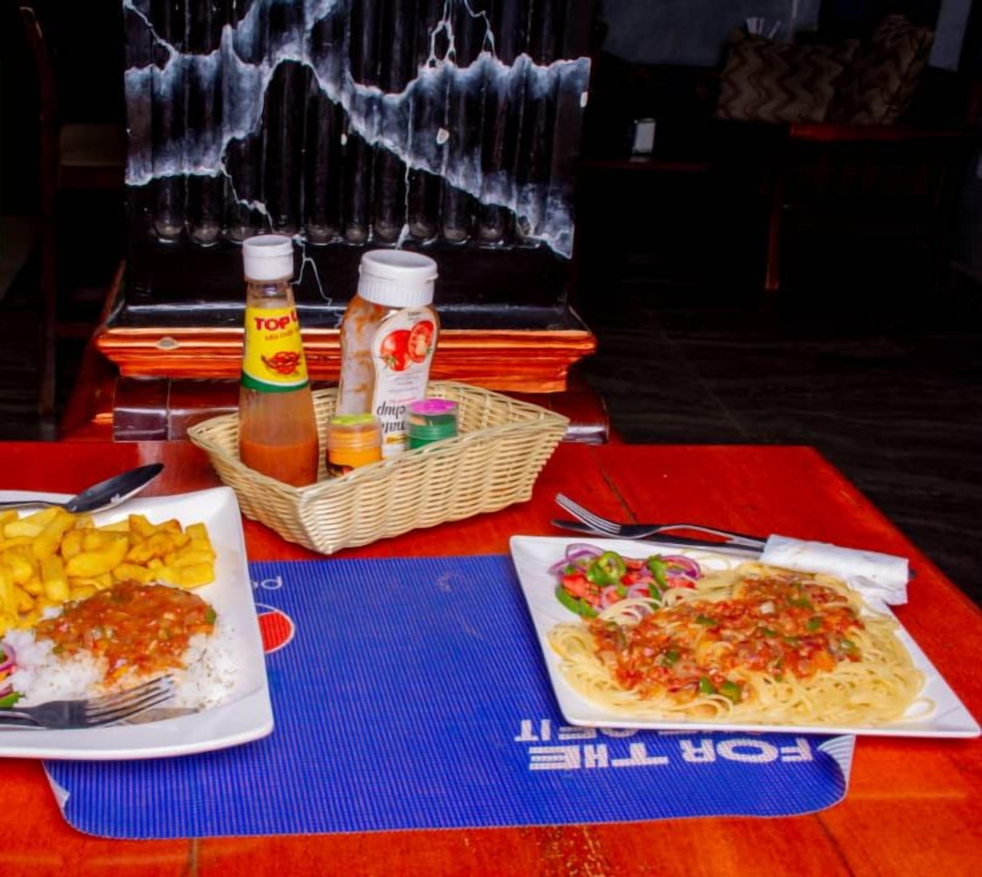 Una mesa de comedor con dos platos de comida, una botella de Topo Chico y una cesta con salsas.