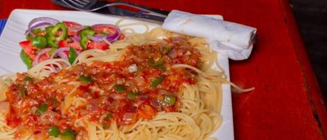 A plate of spaghetti with tomato sauce and vegetables, a fork, and a napkin on a red table with a blue placemat.