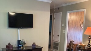 Een woonkamer met een flatscreen televisie, een glazen salontafel en een plafondventilator.