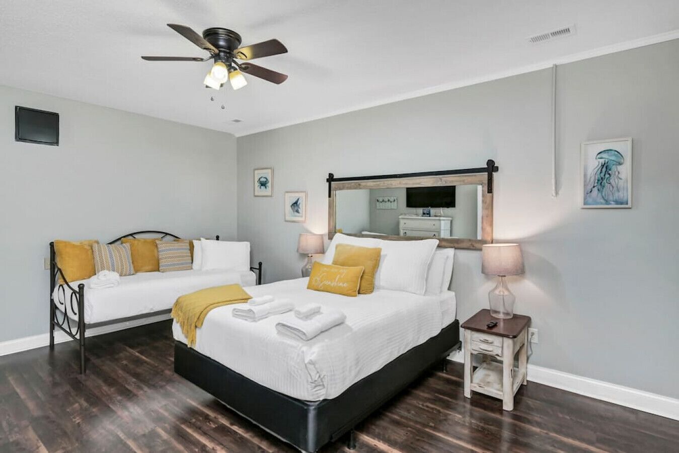 Una camera da letto con due letti, una ventola a soffitto, uno specchio e opere d'arte alle pareti.