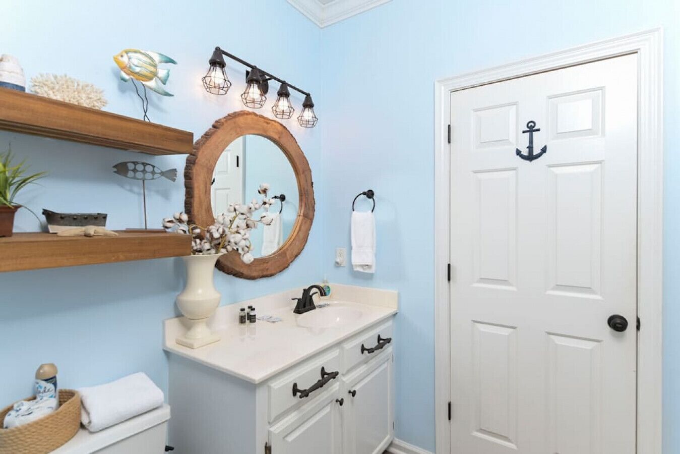Un baño con una puerta blanca, un tocador de madera, un espejo grande y un estante con adornos.