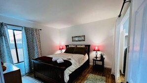 A bedroom with a bed, two bedside tables with lamps, a window with curtains, and a door.