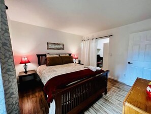 A bedroom with a bed, two bedside tables with lamps, a wooden bench, a door, and a small table with a box. - The Emerald at Mesa (Mesa)