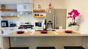 A modern kitchen with white cabinets, a stainless steel refrigerator, and a central island with stools.