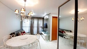 A modern living room with a dining area, a sofa, a TV, and a large mirror. - Flats à beira-mar no Carneiros Beach Resort (Tamandaré)