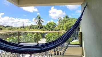 A hammock on a balcony with a view of greenery and a clear sky.