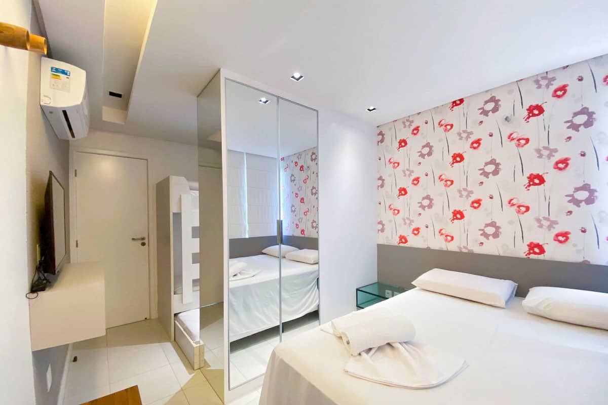 Ein modernes Hotelzimmer mit einem Bett, einem Spiegel, einem Fernseher und floralem Wandpapier.