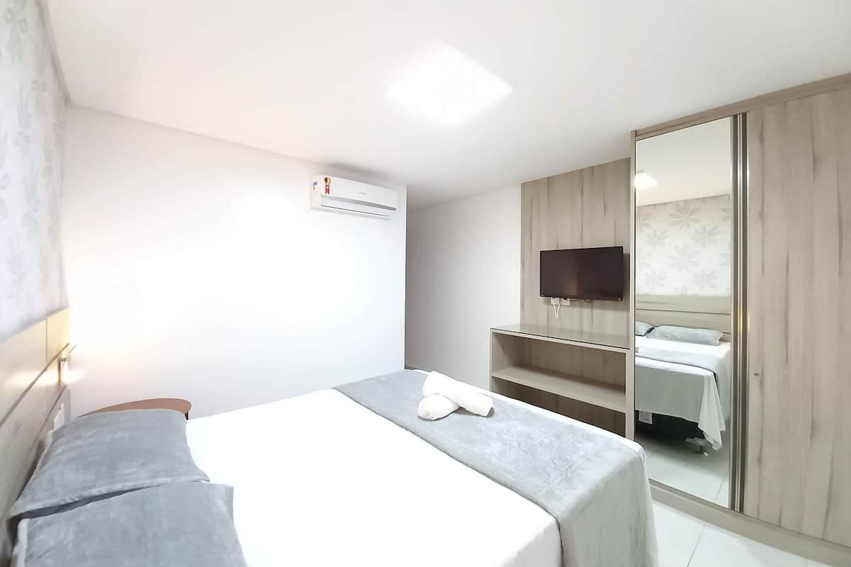 Ein Hotelzimmer mit einem Bett, einem an der Wand befestigten Fernseher, einem Kleiderschrank und einer Klimaanlage.