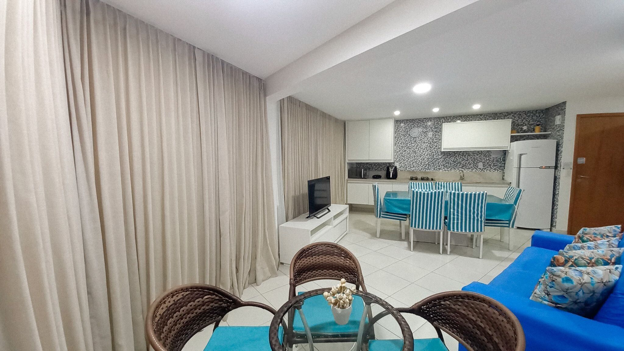 A living room with a sofa, a dining table with chairs, a TV, and a kitchen area with cabinets and a refrigerator.