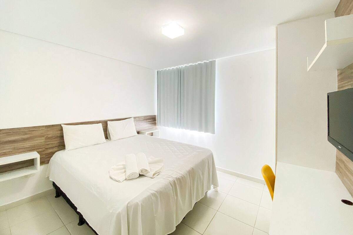 Ein Hotelzimmer mit einem Bett, einem Fernseher, einem Fenster mit Vorhängen und einem Nachttisch.