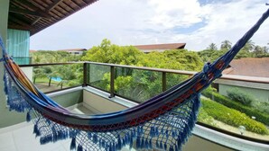 A hammock on a balcony with a view of lush greenery and buildings. - Flats à beira-mar no Carneiros Beach Resort (Tamandaré)