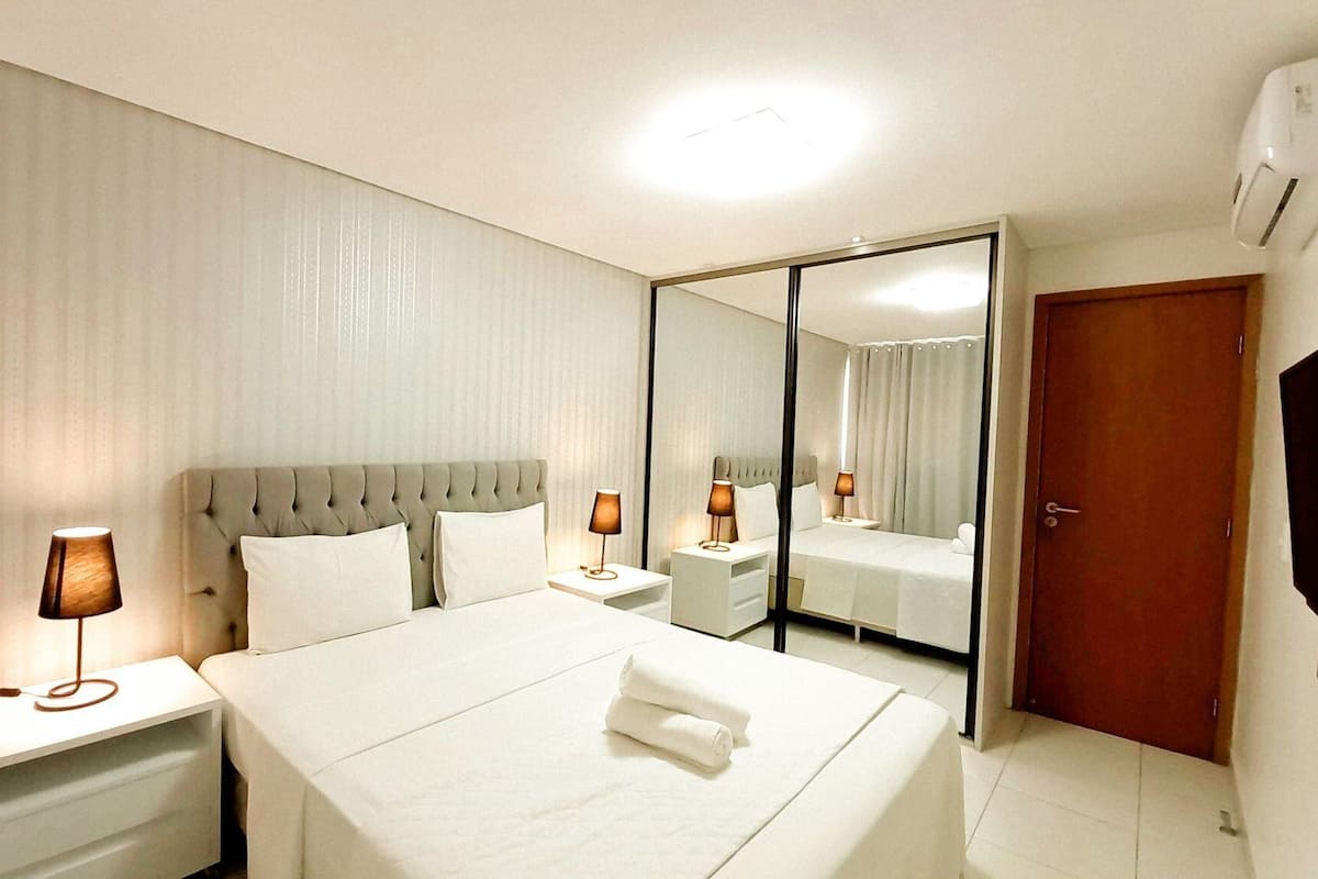 Ein Hotelzimmer mit einem großen Bett, Nachttischlampen, einem Spiegel und einer Tür.