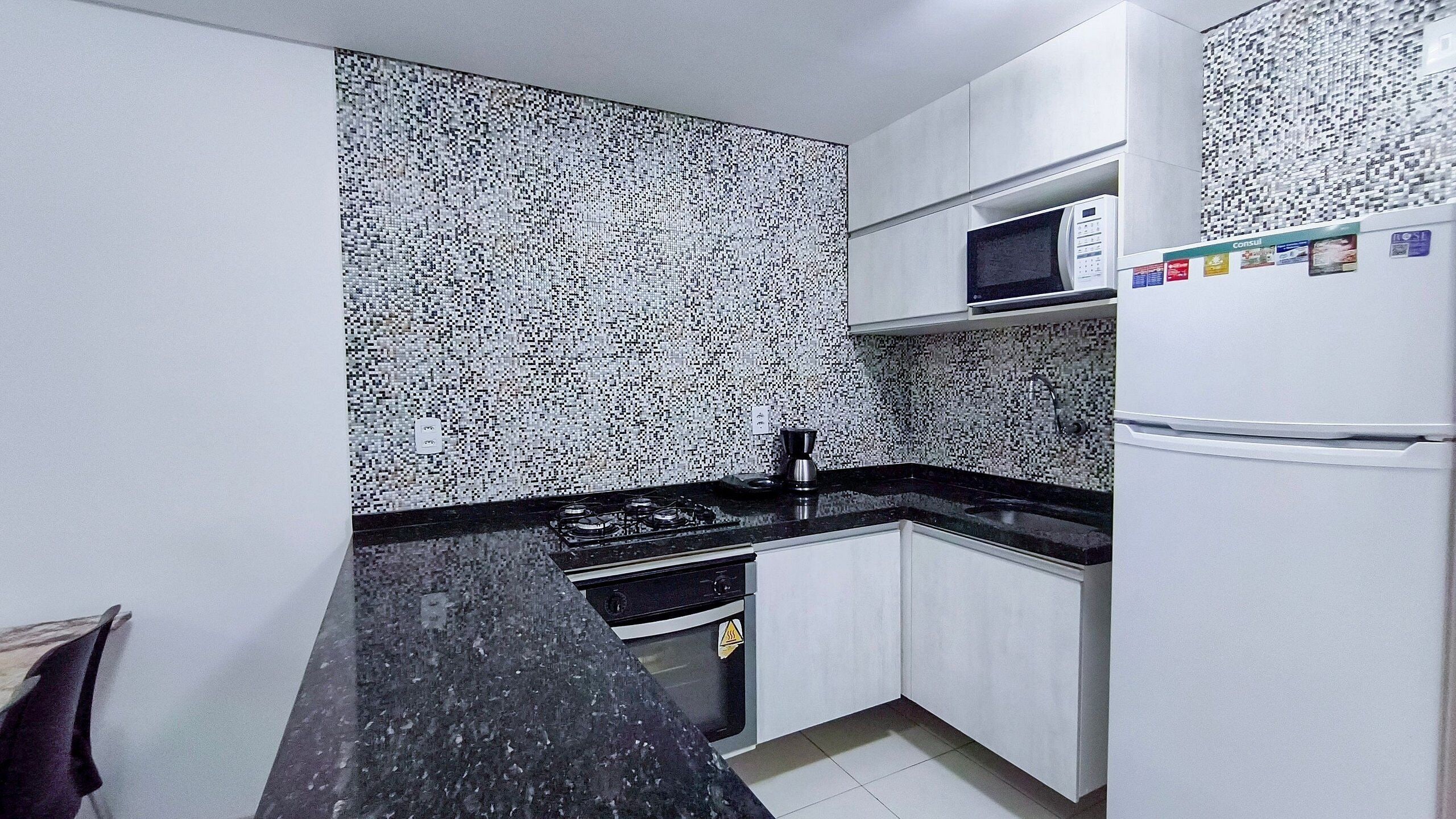 Una cocina con encimera negra, armarios blancos, microondas y refrigerador.