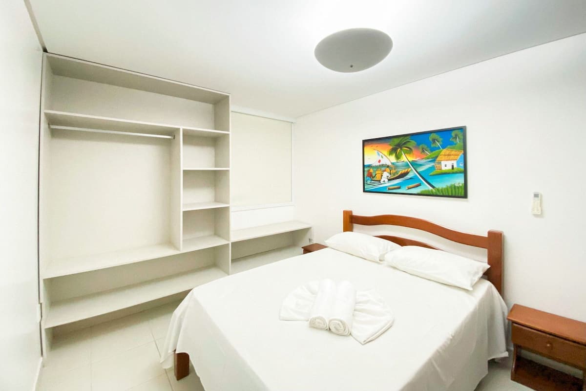 Ein Schlafzimmer mit einem Bett, einem Holz-Kopfteil, einem Nachttisch, einem weißen Kleiderschrank und einem Bild an der Wand.