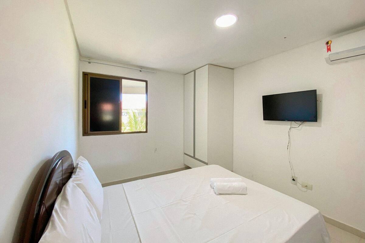 Ein Hotelzimmer mit Bett, einem an der Wand befestigten Fernseher, einem Fenster mit Ausblick und einer Deckenleuchte.