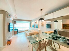 Una cocina moderna con una mesa de vidrio para comer, un sofá y un televisor montado en la pared.